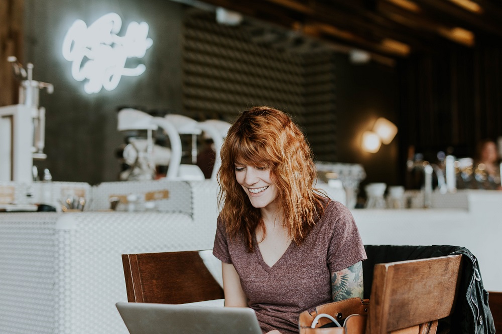 A woman smiling while looking at a laptop screen at a coffee shop