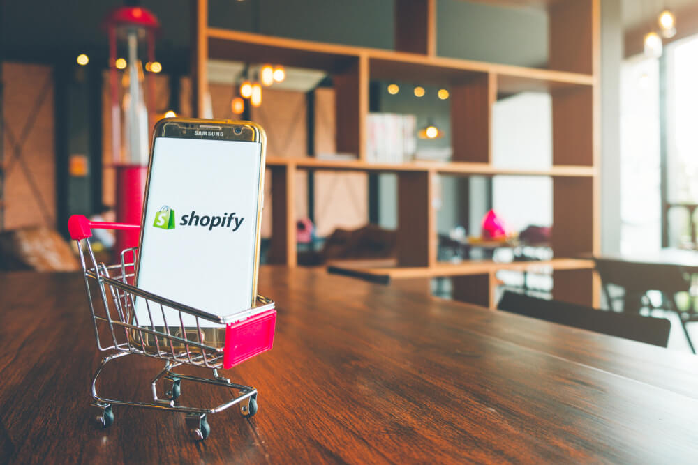 Phone display showing Shopify app on a tiny grocery cart