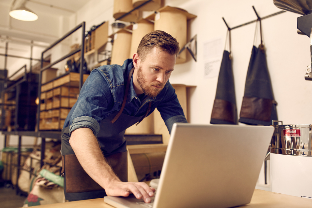 Serious young business owner using laptop in his workshop