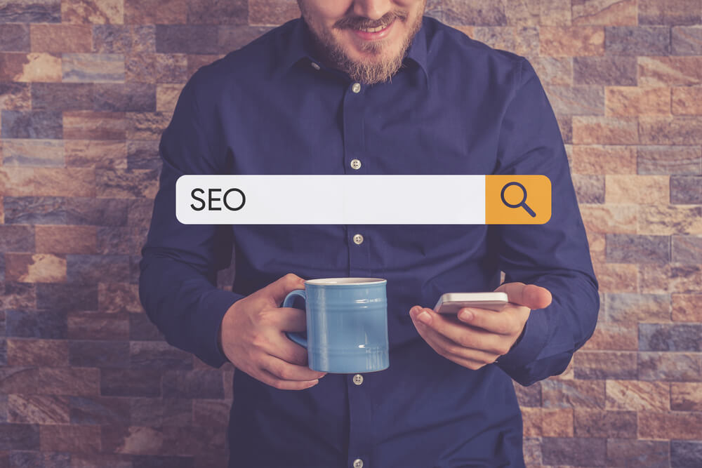 SEO in search bar with man in background holding mug and phone