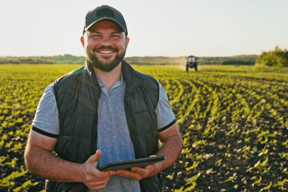 Smiling farmer holding tablet with working tractor in background