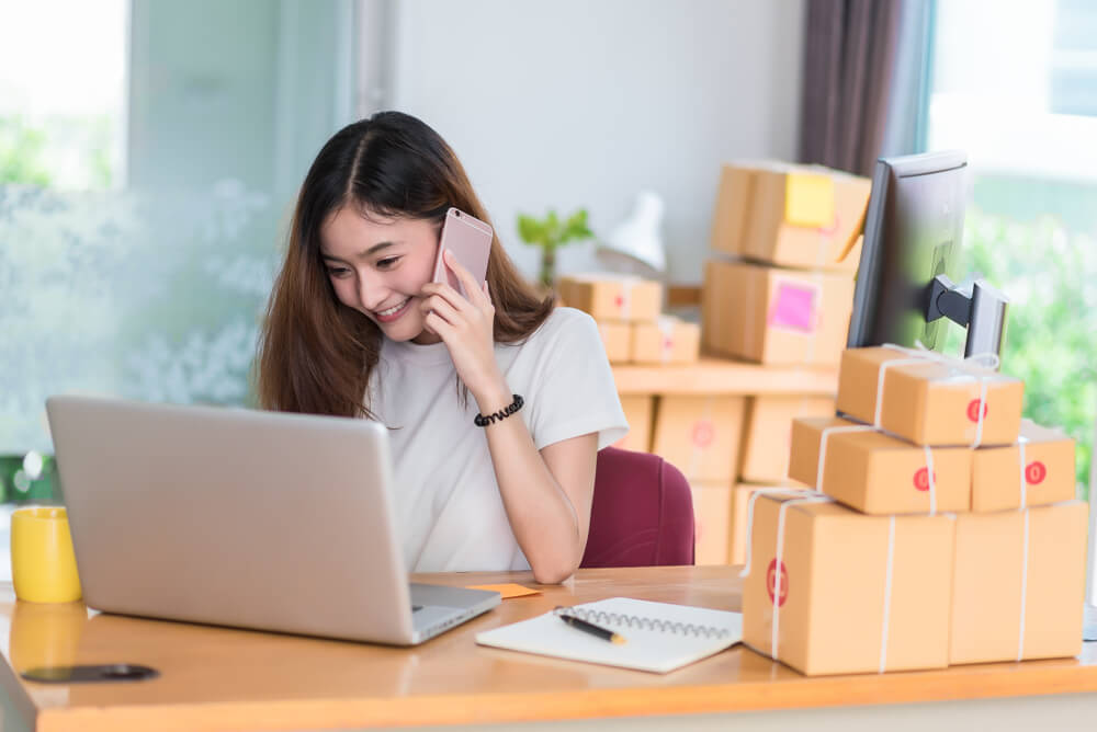 female e-commerce shop owner transacting on phone and laptop