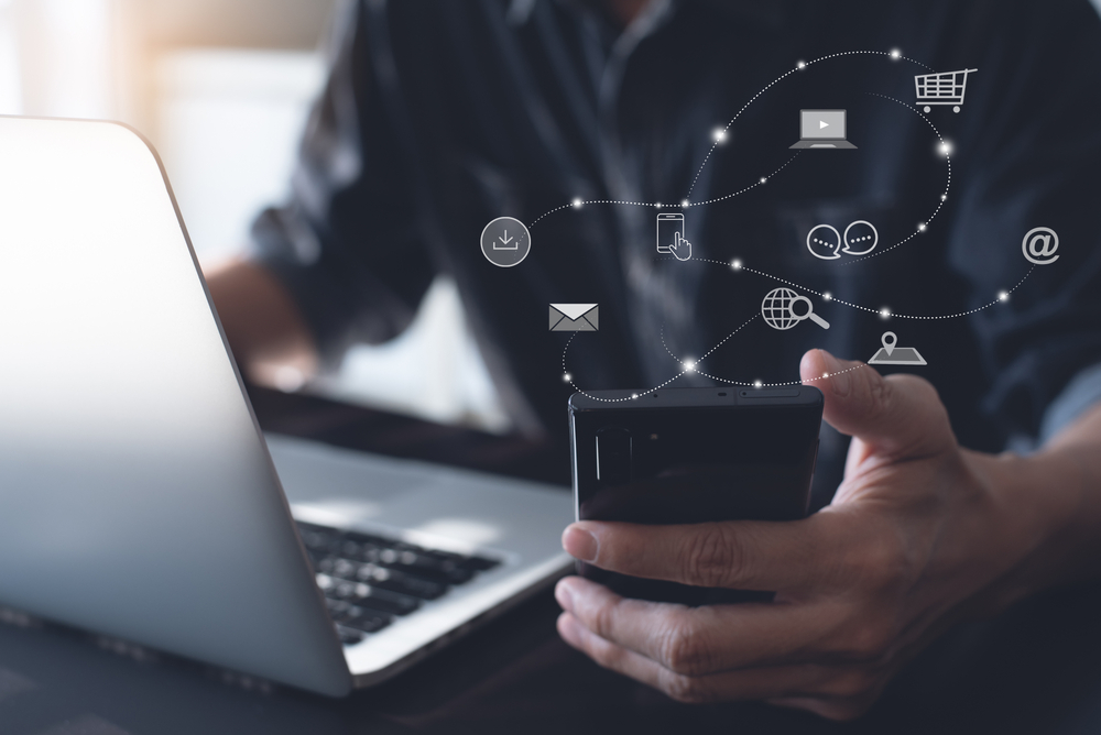 man using laptop and holding smartphone with floating 3d digital marketing icons